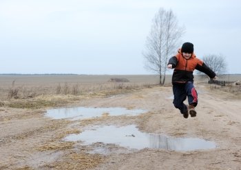 A boy jumps over a puddle on a rural road