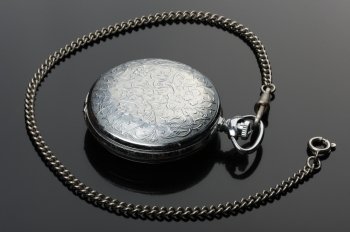pocket watch with closed cover and their reflection on a black background