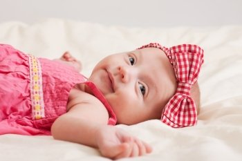 Cheerful baby girl toddler wearing pink dress and bow on bed
