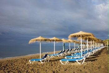 Sun loungers in the morning on a sandy beach by the Mediterranean Sea at the popular resort of Marbella, Costa del Sol, Andalusia region, Spain