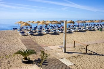 Summer holiday scenery, sandy beach by the blue sea, deckchairs, wooden path and a shower in Marbella resort on Costa del Sol in Spain.