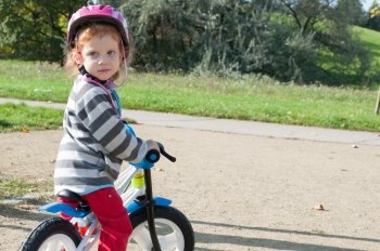 Child girl with the safety helmet on the bike in the autumn park