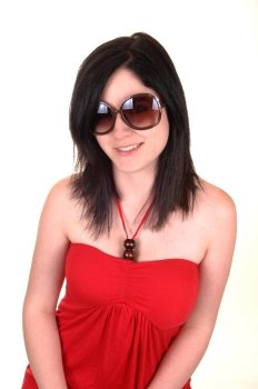 A closeup portrait of a young woman with sunglasses and black hairsmiling into the camera, in a red dress on white background.