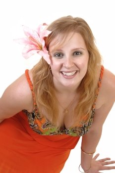 A beautiful blond teenager sitting on the floor, smiling into the camera witha pink lily in her hair and in a colorful orange dress, for white background.