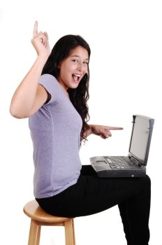 An happy young woman pointing with her finger to her laptop and up inthe air, sitting in black jeans on a chair, for white background. 