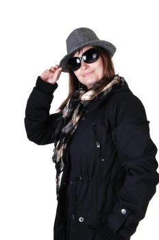 A middle-aged woman in a dark blue winter coat, brown boots and a beigehat with sunglasses and a scarf, standing in the studio for white background.