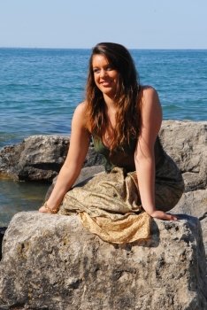 The teenager, representing the earth, dressed in brown and green, sitting on the shore of lake Ontario in bright sunshine and the waves coming to shore.