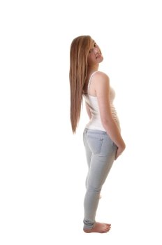 A young pretty teenager in jeans and white t-shirt standing bare feetinto the studio and her long brunette hair hanging down on her back.