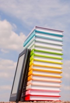 Stack of colorful books and electronic book reader outdoors