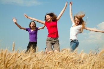 Teen girls jumping at a wheat field in a sunny day