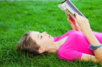 Teen girl reading the Bible outdoors lying on the grass