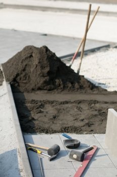 Tiling of pavement and sand pile. Two shovels and Construction tools scattered