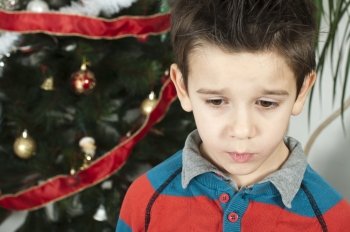 Unhappy little boy on christmass. Christmas tree in the background