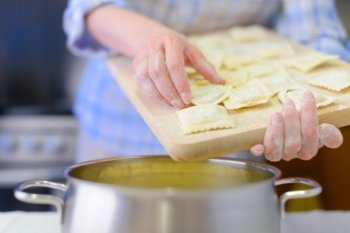 Italian ravioli. Cooking: woman hands holding fresh ravioli over the saucepan