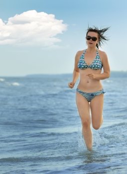 The girl running on seacoast. The European appearance in sunglasses