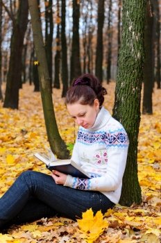 The attractive woman reads the book in autumn forest.