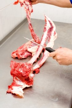 butchers hands cutting meat off beef ribs