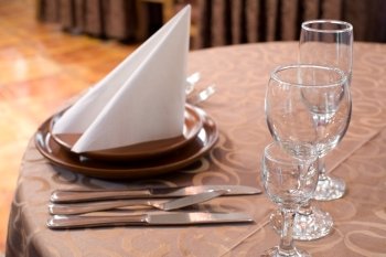 laid restaurant table with light brown tablecloth with brown ware, shallow DOF, focus on glass stemwares