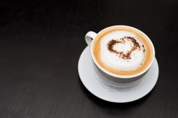 cup of cappuccino coffee on saucer, chocolate heart on top, copy space