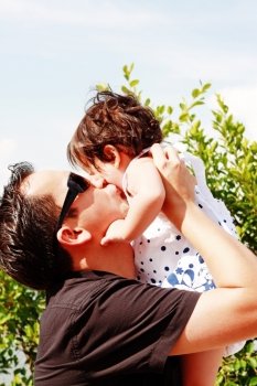 father in early thirties gives his son a kiss on the cheek in the park 