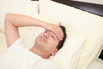 Close up of young man lying down in bed taking temperature and having flu 