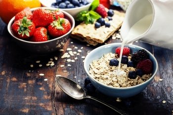 diet breakfast - bowls of oat flake, berries and fresh milk on wooden background - health and diet concept