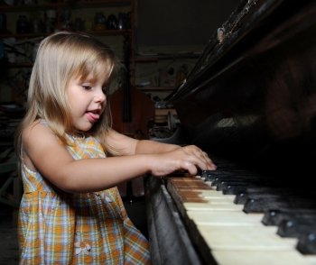 Little girl playing on an old black piano