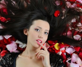 Portrait of beautiful brunette in red rose petals