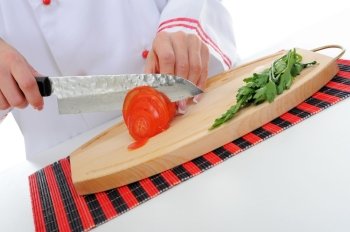 Chef in uniform cuts the tomato in the kitchen. Isolated on white background