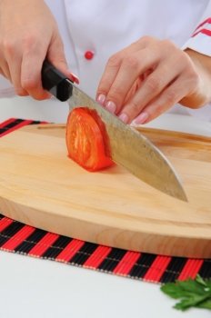 Chef in uniform cuts the tomato in the kitchen.
