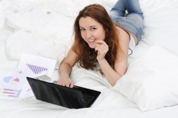 young woman with laptop lying on the bed. Isolated on white background