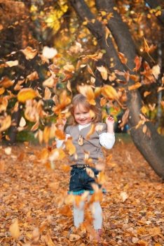 Smiling little girl (3 years) playing with dry autumn leaves. Evening in a park