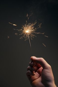Man holding a burning sparkler firework in his hand.