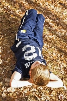 A young boy outside lying in the leaves.