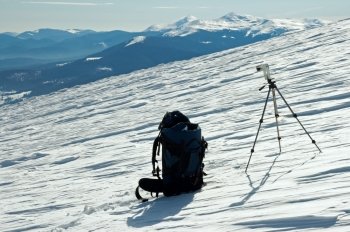 Winter mountain landscape with tourist knapsack and photographic tripod (Ukraine, Carpathian Mt’s, Goverla and Petros Mountains behind)