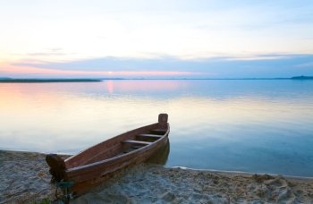 Sunset and old wooden fishing boat near the summer lake shore (Svityaz, Ukraine)
