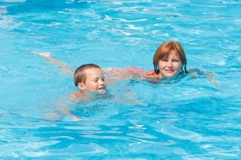 Mother train her son to swim in the summer outdoor pool.