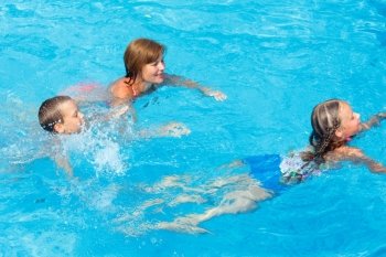 Mother teaches children to swim in the summer outdoor pool.