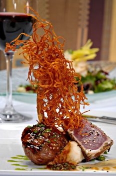 Grilled lamp chop topped with a light sauce and green onions, plated alongside seared ahi tuna over mashed potatoes.  All is topped with deep fried shredded sweet potatoes.
