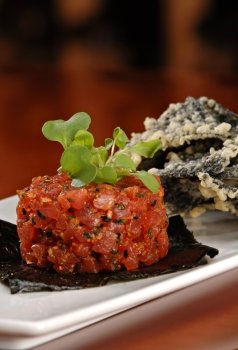 Raw ahi tuna tartare appetizer atop a sheet of nori and garnished with fresh green sprouts. Served with a side of tempura tortilla chips.