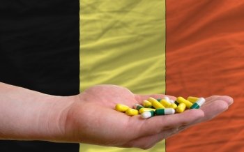 man holding capsules in front of complete wavy national flag of belgium symbolizing health, medicine, cure, vitamines and healthy life