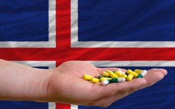 man holding capsules in front of complete wavy national flag of iceland symbolizing health, medicine, cure, vitamines and healthy life