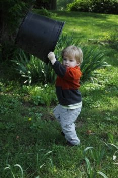 Toddler boy holding a large planter pot over his head in the back yard