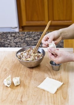 Women’s Hands making wonton with wooden board and stainless steel bowls in kitchen