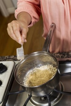 Women adding Wheat Germ to Oatmeal Breakfast while cooking on stove top 