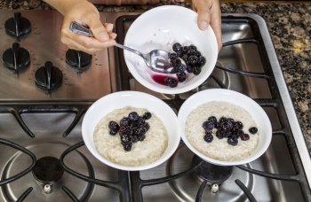 Blueberries being added to Oatmeal Breakfast in white bowls on stove top 