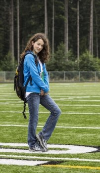 Young girl holding notepads on soccer field with woods in background