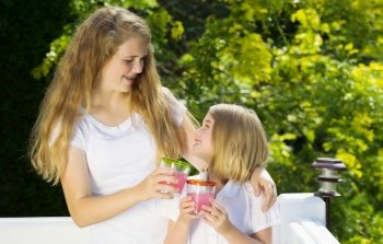 Side view of sisters hugging each other while drinking cold lemonade outdoors on patio 