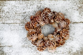 Natural pine cone wreath on snow and rustic wood setting the holiday mood 