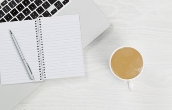 High angle view of laptop, coffee and blank notepad with silver pen on rustic white desktop. 

